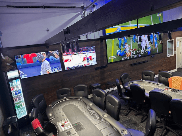 A poker table with multiple TVs showing sports events above it.